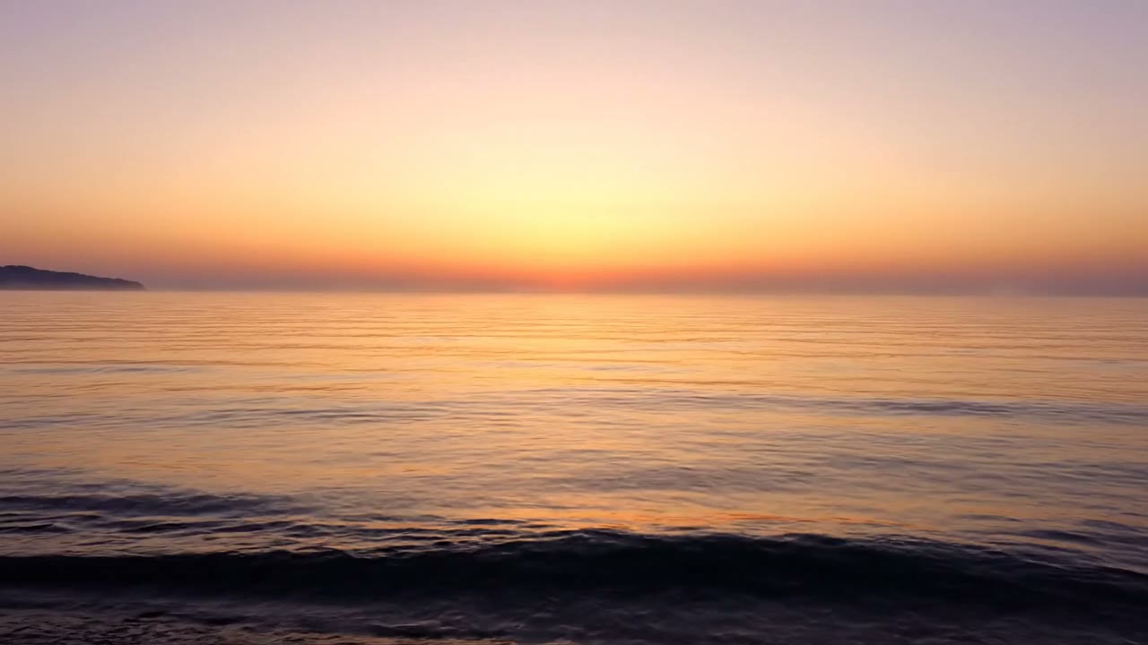 A calm sea at sunrise, soft golden light on still water